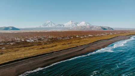 A panoramic shot of a beautiful field with the sea on the side and amazing mountains in the backgroundの写真素材