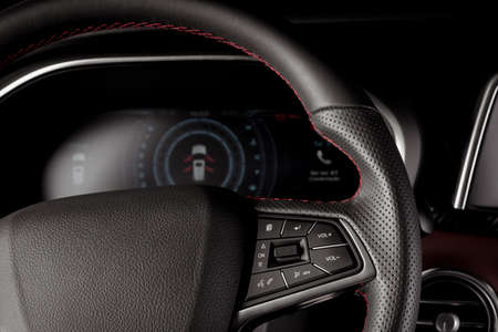 A closeup of the eather-covered steering wheel of a new SUV car against the digital speedometer