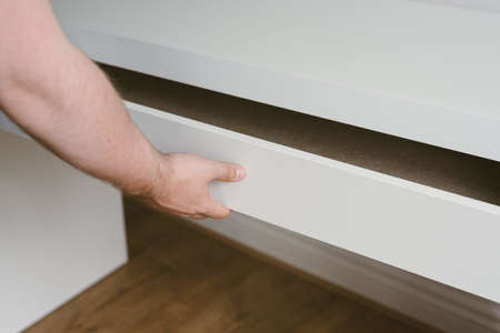 A shot of a young Caucasian male hand fixing drawers or shelves indoors