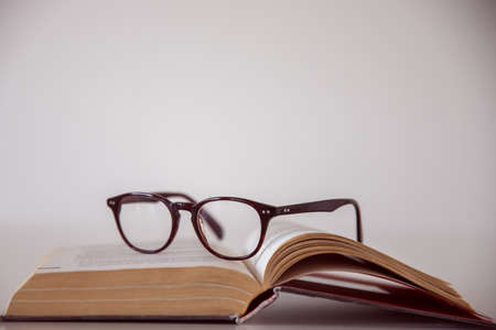 A pair of glasses on an open book with a white backgroundの写真素材