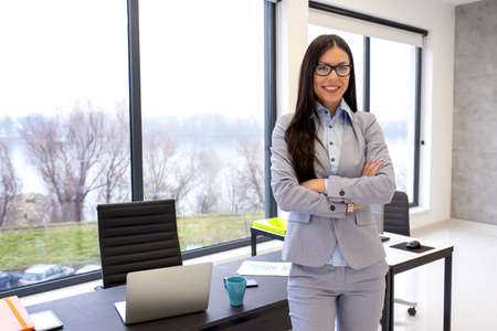 A young businesswoman leaning on her working desk with crossed arms - female entrepreneurship conceptの写真素材