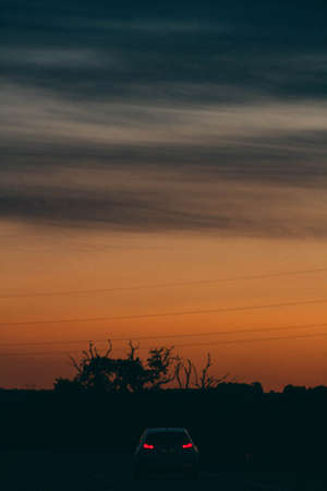 A vertical shot of a beautiful sunset with a car with lights on