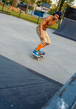A vertical shot of a shirtless young male skateboarding in the park at daytimeの写真素材