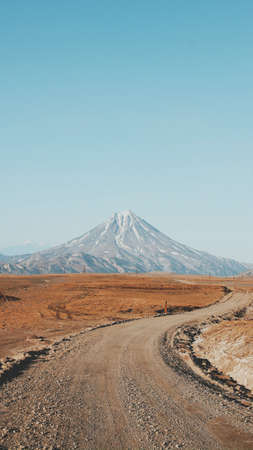 A beautiful vertical shot of a narrow curvy and muddy road with an amazing high mountain in the...