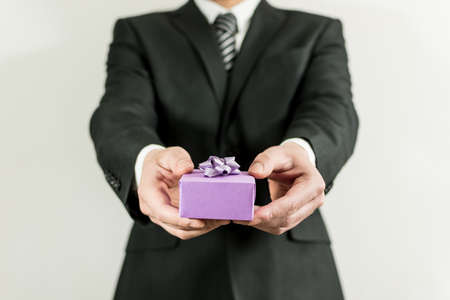 A person in a suit holding a purple small present boxの写真素材