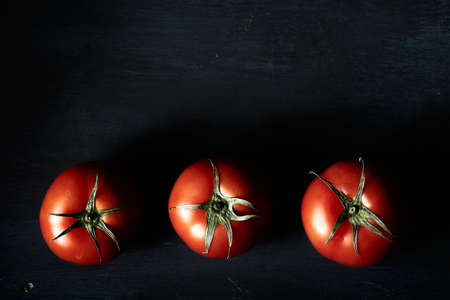 A high angle closeup shot of three fresh tomatoes on a black background