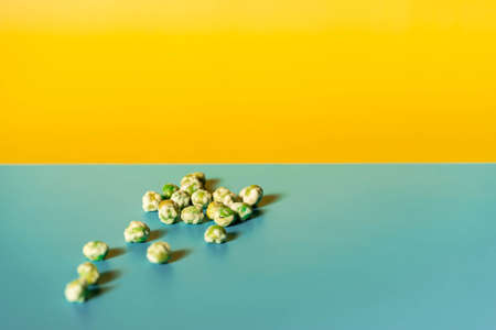 A closeup shot of green wasabi peas on a blue yellow background