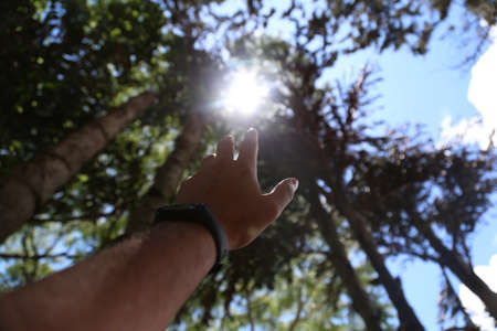 A male reaching towards the sun with blurred natural backgroundの写真素材