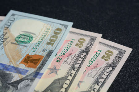 A closeup shot of a hundred and two fifteen united states dollars on a dark gray backgroundの写真素材