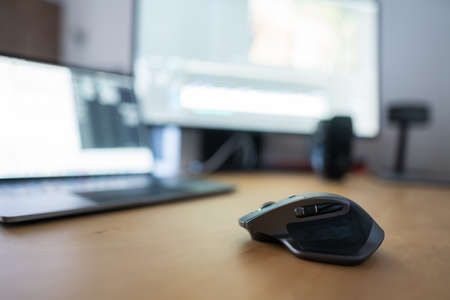 A closeup of a gaming mouse with a blurred laptop and a monitor in the background