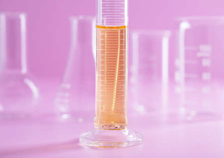 A closeup shot of a measuring cylinder flask with yellow liquid on a pink background at a lab