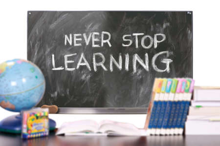 A closeup shot of a blackboard with the text "never stop learning" and books, a globe in frontの写真素材