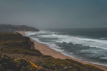 An aerial shot of the beautiful sandy coast of the sea with a dark grey skyの写真素材