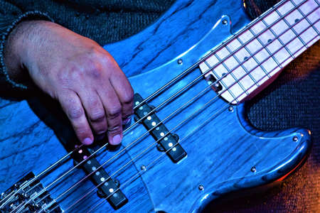 A closeup shot of musician hands playing the blue bass guitar