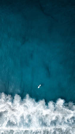 An aerial overhead vertical shot of beautiful ocean waves with a plane flying aboveの写真素材