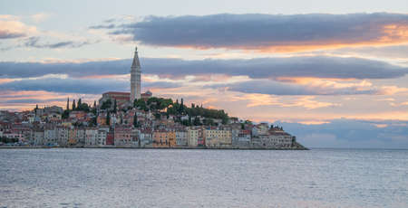 A coastal town in far distance next to the calm sea during sunset with clouds and the skyの写真素材