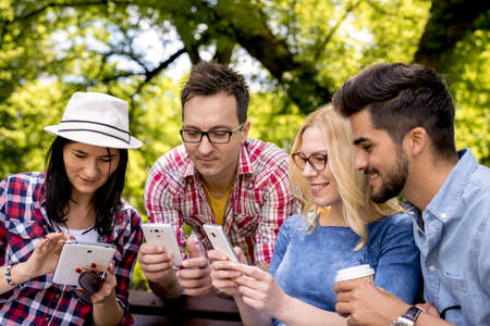 A group of Caucasian friends playing with smartphones in the park