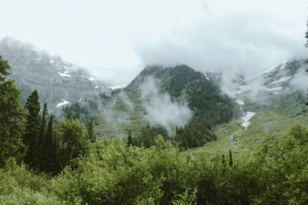 A forested mountains in a fog with snow on them at Glacier National Park, Montana, USA