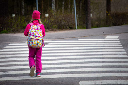 A teenager in a pink outfit with a cute backpack crossing the zebra on the street at daytimeの写真素材
