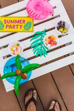 A high angle shot of sweet snacks and inflatable pool cup holders with the tag SUMMER PARTY on a...