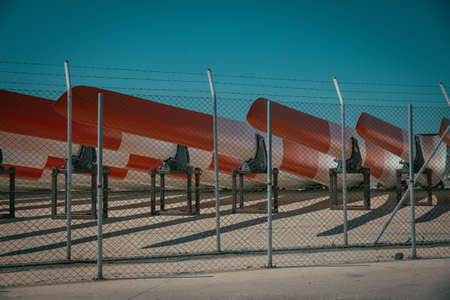 A metal fence with barb wire and metal canoes behind it with blue sky in the background