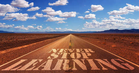 A closeup shot of a straight highway with a painted note Never stop learning on the foreground