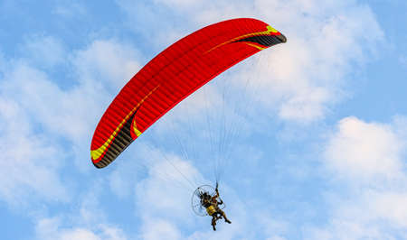 Red dome of a motor paraglider flying on a background of blue cloudy summer sky. Tandem on a paraglider high in the sky.の写真素材