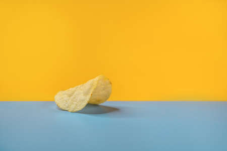 A closeup shot of a single plain potato chip on a yellow blue backgroundの写真素材