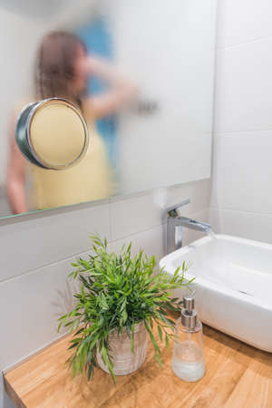 A vertical shot of the reflection of young caucasian female on a moist mirror