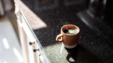 A wide closeup focused shot of a cup of black coffee on a kitchen shelf in the morningの写真素材
