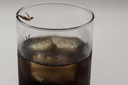 A miniature figurine jumping into a glass of alcohol filled with ice cubes on a white background