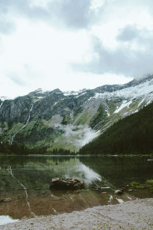 A vertical shot of a rock in Avalanche Lake, with a forested mountain in the background at Glacier National Park, Montana, USAの写真素材