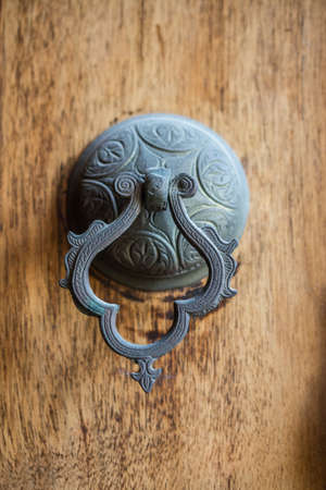 A vertical image of a vintage brass door knocker on a wooden door