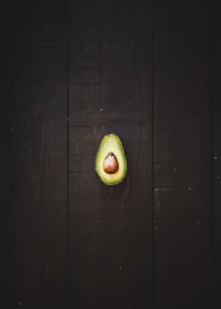 A minimalistic shot of half-sliced avocado from the top with dark brown wooden backgroundの写真素材