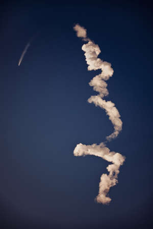A vertical shot of white trails left after an airplane in a clear blue skyの写真素材