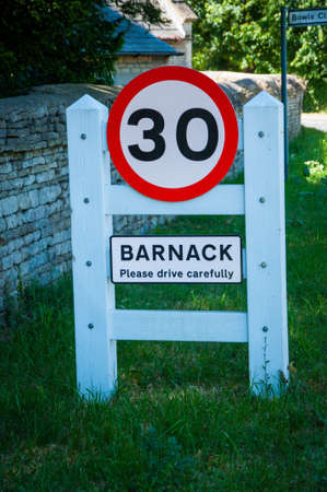 A vertical shot of a sign on the green grass of the Barnack Village, UK