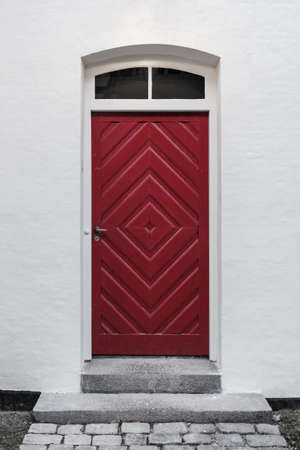 A red designer-made door perfectly in the center on a white wallの写真素材