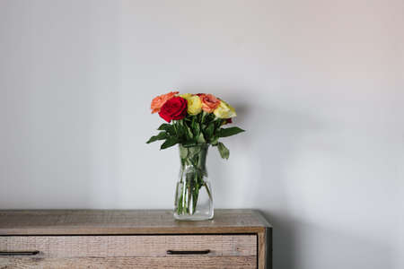 A beautiful bouquet of colorful roses in a glass jar on a wooden cabinet