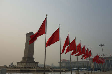 A long range shot of Chinese flags with a monument and smoggy sky in the background in Beijing, Chinaの写真素材