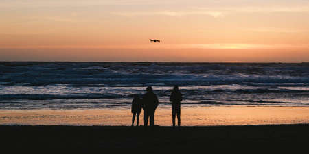 Silhouettes of people standing on the beach and enjoying the beautiful sunset on the horizonの写真素材