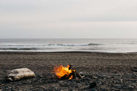 A bonfire at the beach with a cloudy grey sky in the backgroundの写真素材