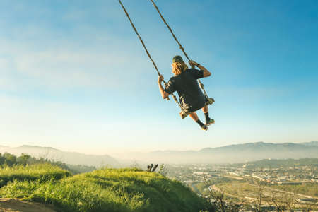 A wide shot of a person swinging on a swing near grass under a clear skyの写真素材