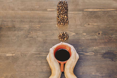 A high angle shot of a cup of coffee near coffee beans on a wooden tableの写真素材