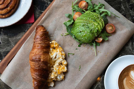 A high angle shot of a fresh croissant with eggs and avocadoes on a parchment paperの写真素材