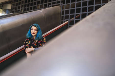 A beautiful Caucasian female with blue hair posing on an escalator in an old building