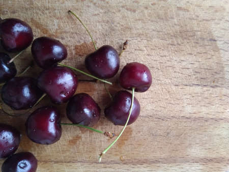 A high angle shot of fresh cherries on a wooden board under the lights