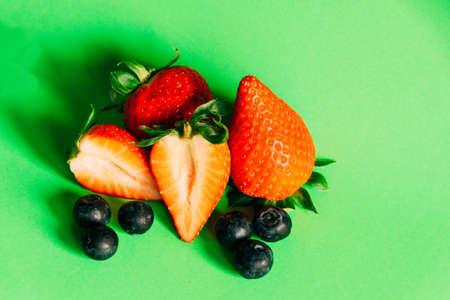 A top view of fresh blueberries and strawberries isolated on a green background