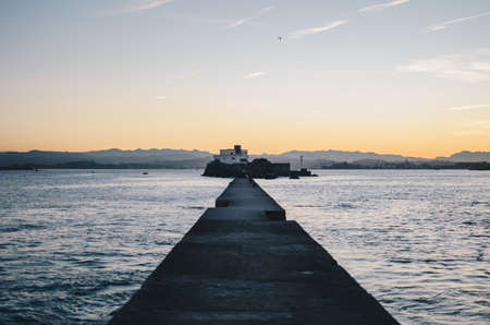 The beautiful dock of the coastal city with a little island and beautiful hills in the background at sunriseの写真素材