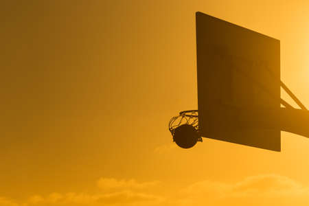 Basketball in a hoop with the sun shining from an angleの写真素材