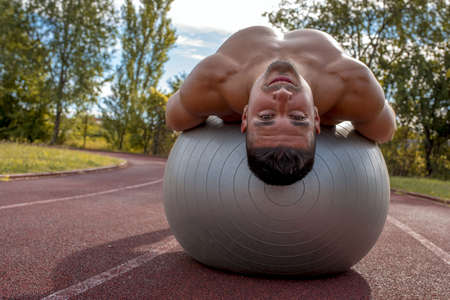 A Caucasian muscular shirtless fitness man exercising with fitness ball outdoor in a parkの写真素材